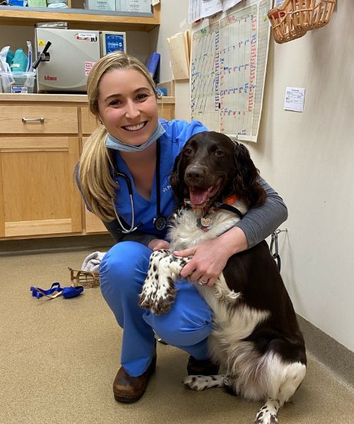 A woman in scrubs kneeling down, gently interacting with a dog.